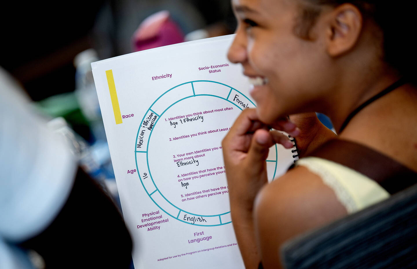 A person smiles while holding a worksheet that explores various identities such as race, ethnicity, age, and language.